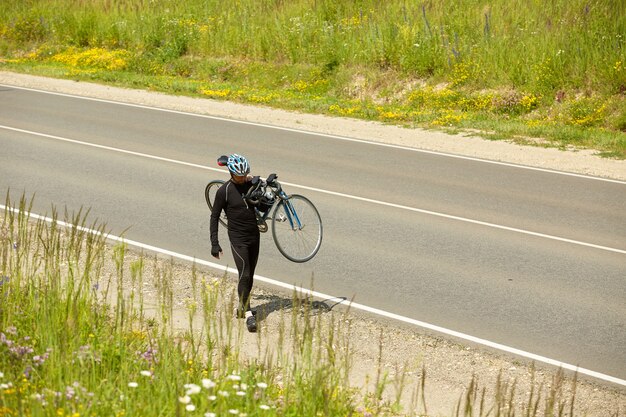 Foto de un atleta de triatlón llevando su bicicleta en una carretera abierta