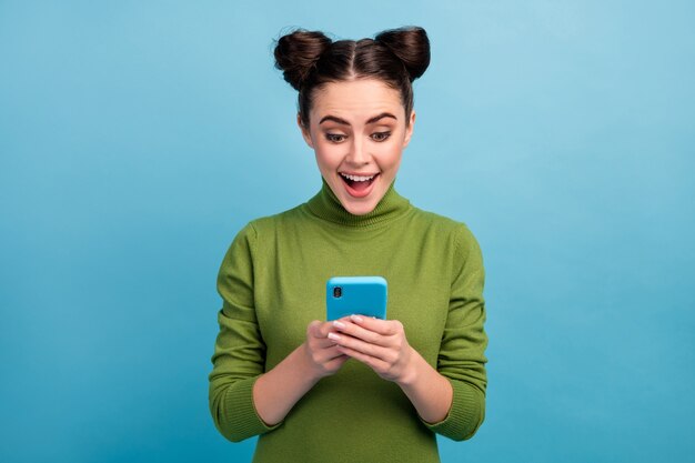 Foto de atractiva bonita dama adolescente con la boca abierta charlando navegando por teléfono leer publicación de blog adicto usuario de teléfono inteligente usar cálido cuello alto verde aislado pared de color azul