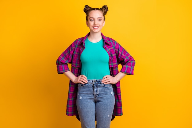 Foto de atractiva dama adolescente bastante encantadora dos divertidos bollos tomarse de las manos a los lados persona segura de sí misma buen humor desgaste casual plaid magenta camisa jeans aislado fondo de color amarillo brillante