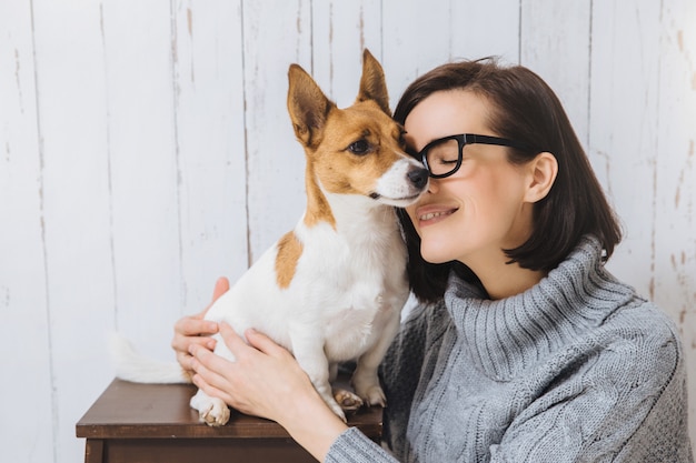 Foto de atractiva joven abraza a su perro favorito, toca con la nariz, expresa un gran amor a la mascota. Perro leal tiene buenas relaciones con el anfitrión. Amistad, relaciones, animales y personas