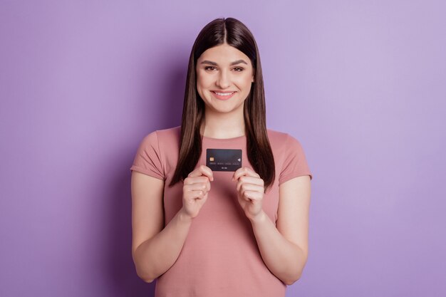 Foto de la atractiva joven feliz sonrisa positiva sosteniendo la tarjeta bancaria comprar tienda aislada de fondo de color violeta