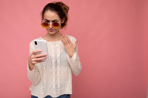 Foto de atractiva joven insatisfecha vistiendo casual blusa blanca y gafas de sol coloridas