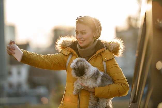 Una foto de una atractiva joven y su perro pasando tiempo en la calle de la ciudad y haciéndose un selfie.