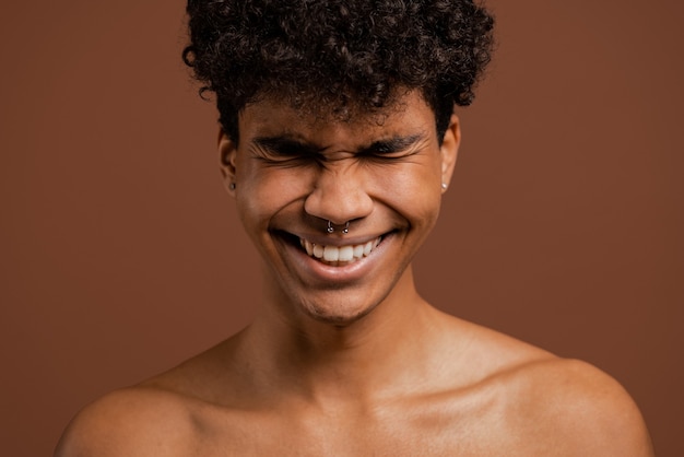 Foto foto de atractivo hombre negro con penetrantes sonrisas con los ojos cerrados. torso desnudo, fondo de color marrón aislado.