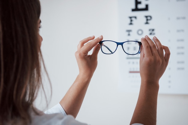 Foto de atrás. Mujer mirando a través de la tabla optométrica de gafas.