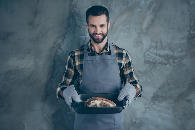 Foto de barbudo buen cocinero profesional alegre habiendo terminado de cocinar el pan y servir esto a la mesa muro de hormigón de pared de color gris aislado