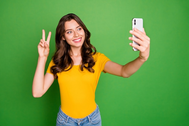 Foto de bastante curly ly sosteniendo el teléfono haciendo selfies mostrando el símbolo v-sign saluda