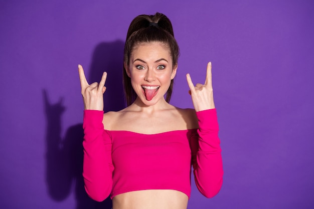 Foto de bastante joven levantar dos brazos mostrar cuernos sacar la lengua use rosa recortada superior aislado de fondo de color violeta