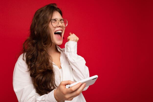 Foto de bastante sonriente joven morena positiva vistiendo camisa blanca y gafas ópticas