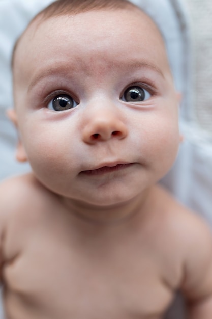 Foto de bebé feliz mirando a la cámara mientras está acostado sobre una sábana blanca en casa.