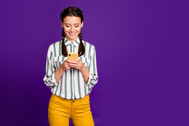 Foto de bella dama sosteniendo el teléfono escribiendo nueva publicación de instagram positivo buen humor desgaste camisa a rayas pantalones amarillos fondo de color púrpura aislado