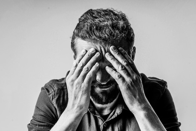 Foto foto en blanco y negro de un hombre que parece extremadamente triste y deprimido. está sentado sobre un fondo blanco y tiene la cara cubierta con ambas manos, mostrando la desesperación y la desesperanza que siente.
