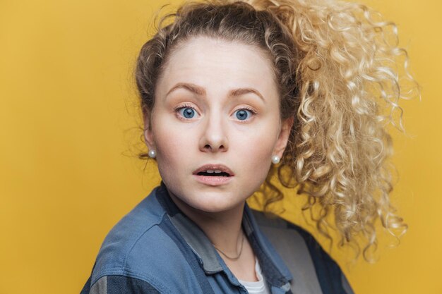 Una foto en la cabeza de una atractiva mujer de ojos azules desconcertada tiene una expresión atónita que no puede entender lo que debería hacer mira con perplejidad directamente a la cámara aislada sobre un fondo amarillo