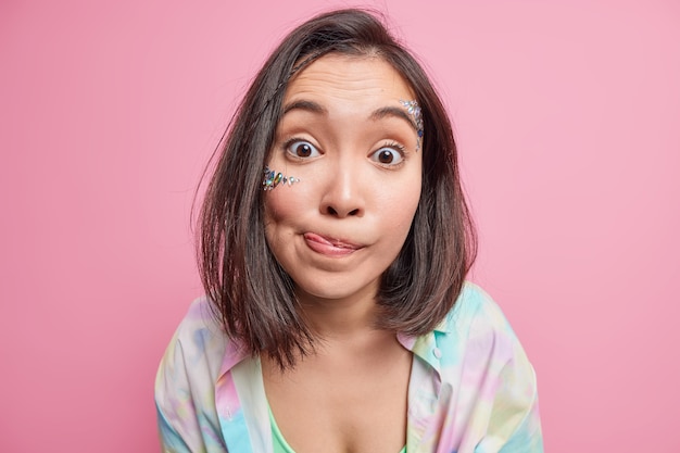 Foto foto de cabeza de una mujer asiática joven morena sorprendida lame los labios mira algo delicioso viste una camisa colorida casual aislada sobre la pared rosada. concepto de expresiones de rostro humano de personas