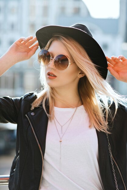 Foto de la calle de la joven encantadora mujer con gafas de sol y sombrero negro