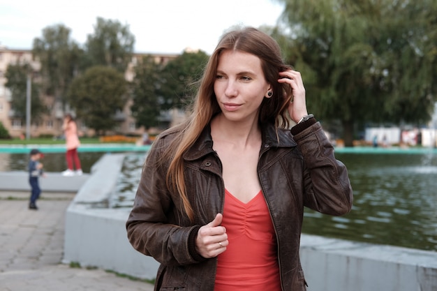 Foto callejera de linda chica pelirroja con vestido rojo y chaqueta de cuero