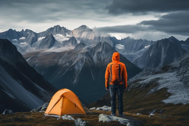 foto caminhante de pé na tenda laranja da frente do acampamento e mochila nas montanhas