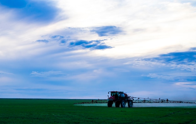 Foto de un campo de trigo rociar un tractor con preparados agroquímicos o agroquímicos sobre un youn