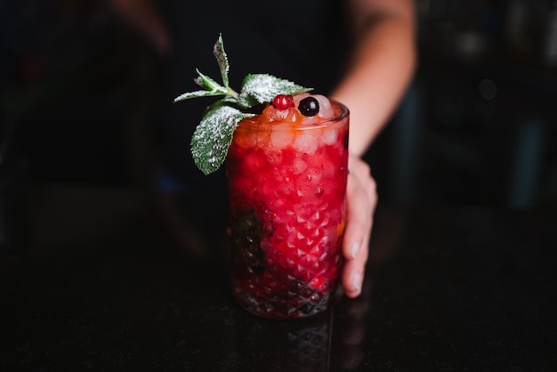 Foto de un cantinero sosteniendo un cóctel de mojito de bayas para dárselo al cliente