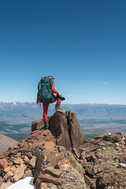 Foto de caza en lo alto de las montañas. Fotógrafo con una gran mochila al borde de un acantilado. Vista vertical.