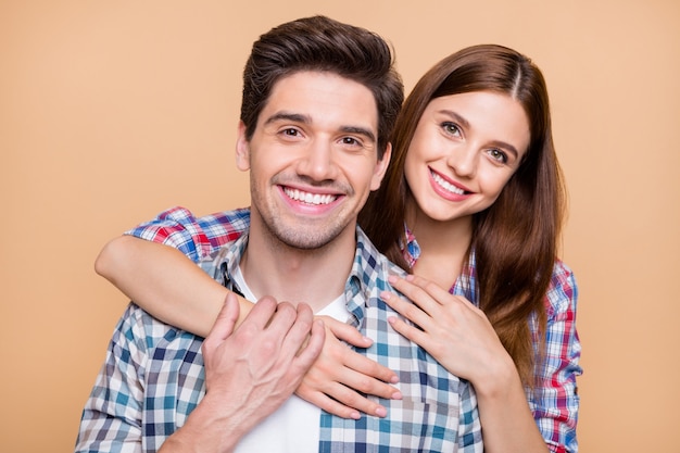 Foto de cerca de la alegre linda pareja positiva de dos personas blancas sonriendo dentudamente amándose con cariño admirando la compañía aislada sobre fondo de color beige pastel