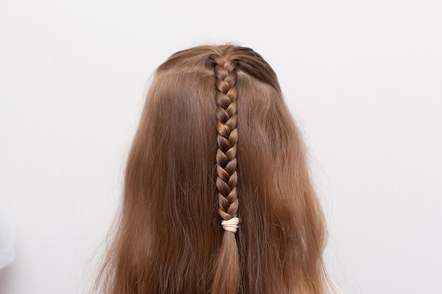 Foto foto de cerca de la cabeza de una niña pequeña con cabello rubio y las manos de la madre cepillándose el pelo y haciendo una trenza o una coleta la madre prepara al niño para el jardín de infantes o la guardería rutina matutina familiar en el baño