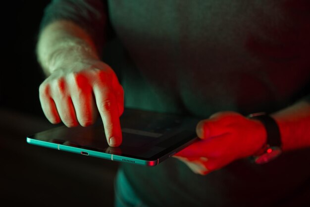 Foto de cerca de un dedo de un hombre tocando una pantalla de tableta digital en luz roja