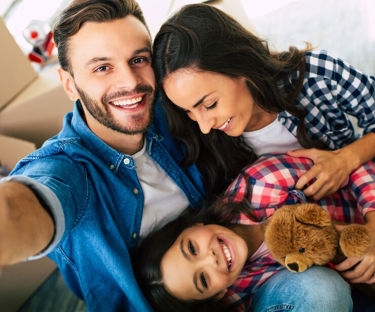 Foto foto de cerca, la familia alegre está tomando selfie juntos en su nueva casa frente a una pila de cajas de cartón