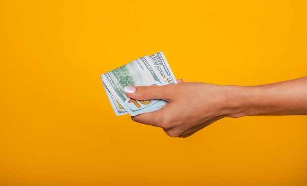 Foto de cerca de hermosas manos femeninas sosteniendo el montón de dólares de Estados Unidos aislado sobre fondo amarillo. Concepto de economía, negocios y finanzas