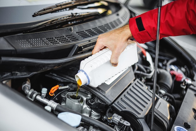 Foto de cerca de una mano mecánica masculina mientras cambia y vierte la calidad del aceite en el motor del automóvil híbrido. Concepto de engranaje de mantenimiento de auto en servicio de reparación