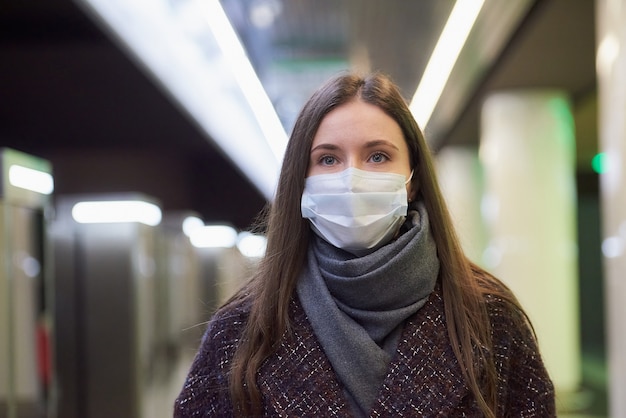 Una foto cercana de una mujer con una mascarilla médica esperando un tren en la plataforma del metro