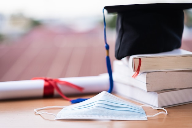 Foto cerrada de un birrete de gorra de graduación universitaria con certificado de diploma de grado y mascarilla sobre la mesa. Graduación en la era de COVID-19