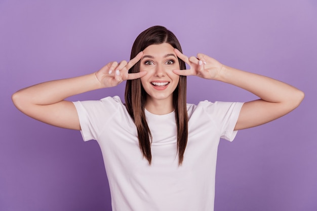 Foto de una chica atractiva que muestra los ojos de la cara con signo v aislado sobre fondo violeta