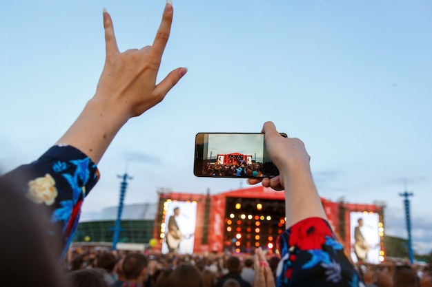 Foto chica disfrutando de concierto de rock, mano levantada y aplausos de placer, disparando con smartphone