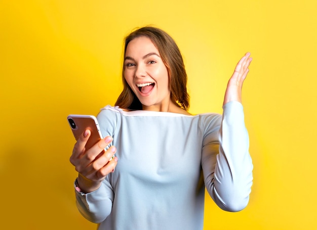 foto de chica emocionada muestra pantalla de teléfono móvil y grito con fondo amarillo