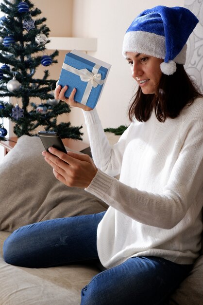 Foto de chica positiva escribiendo una carta en el smartphone sentarse en el sofá de la comodidad en casa en el interior con Navidad