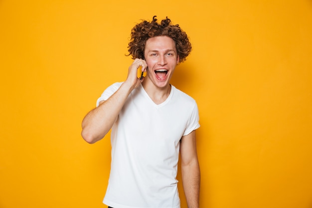 Foto de chico alegre morena con el pelo rizado hablando por teléfono inteligente