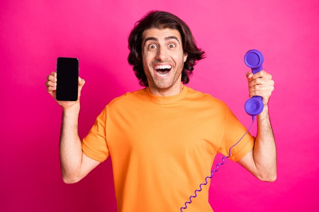 Foto de chico emocionado con la boca abierta sostenga la pantalla del teléfono inteligente teléfono espacio vacío use camiseta naranja fondo de color rosa aislado