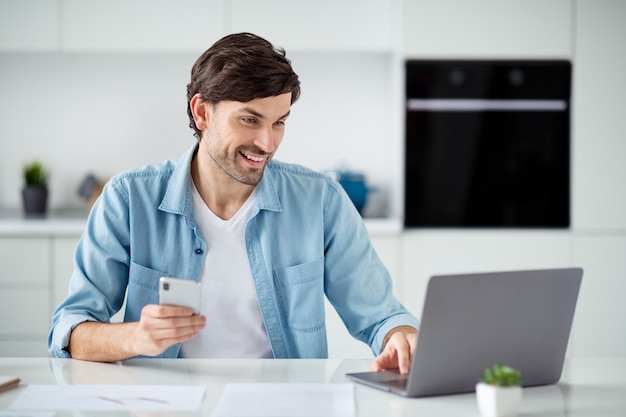 Foto de chico guapo navegando en casa de trabajo del profesor portátil charlando teléfono preparando seminario web