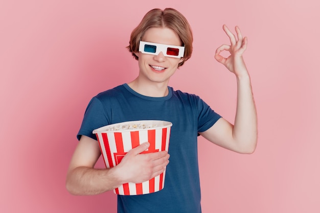 Foto de chico mantenga caja de papel de palomitas de maíz feliz sonrisa positiva use gafas 3d muestran bien un signo de anuncio aislado de fondo de color rosa