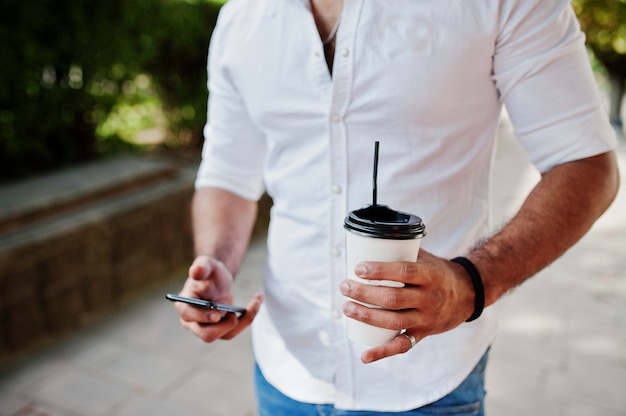 Foto de chico con taza de café y teléfono móvil en las manos de cerca