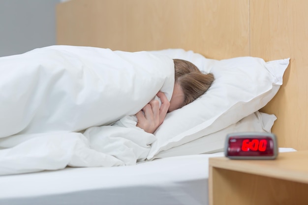 Foto de cierre de una mujer insomne y molesta acostada en la cama debajo de una manta tratando de conciliar el sueño