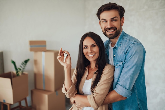 Foto en la cintura de una dama inspirada y un hombre alegre abrazándose y sosteniendo las llaves de su nuevo apartamento