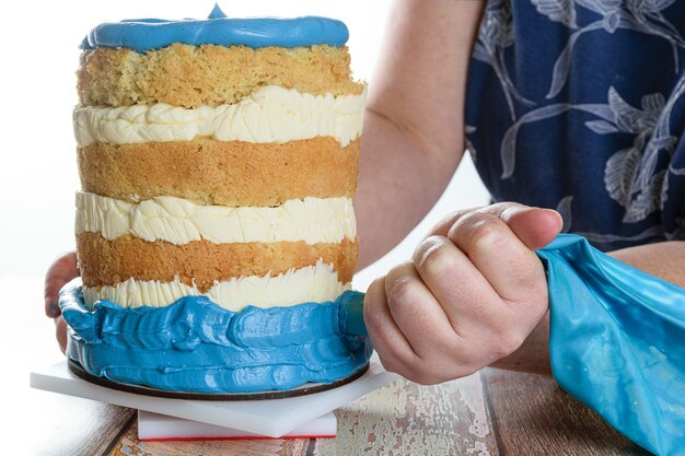 Foto de clave alta. Baker usando una boquilla de glaseado para poner glaseado azul en la base del pastel.