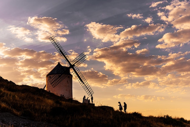 Foto foto com coopy space de pessoas caminhando ao redor de um antigo moinho de vento em uma colina durante o pôr do sol em consuegra, espanha