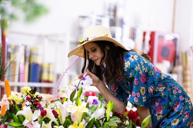 Foto com cópia de uma mulher com chapéu de palha cheirando flores em uma floricultura