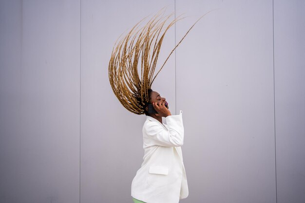 Foto com movimento de uma mulher afro movendo o cabelo para trás enquanto fala com o celular ao ar livre