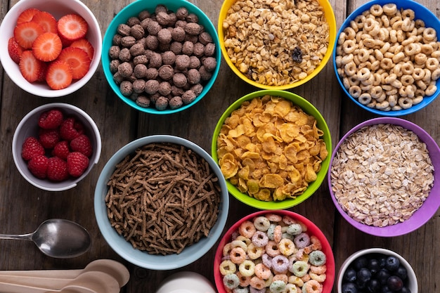 Foto foto completa de frutas vermelhas com vários cereais matinais em tigelas coloridas dispostas na mesa. inalterado, café da manhã, espaço de cópia, variação, comida saudável, lanche e conceito de comida.