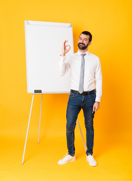 Foto completa do empresário dando uma apresentação no quadro branco sobre amarelo mostrando sinal okey com os dedos