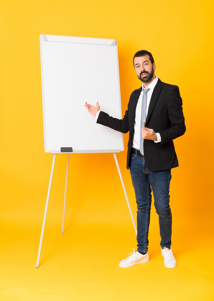 Foto foto completa do empresário dando uma apresentação no quadro branco sobre parede amarela isolada